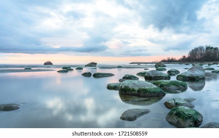 Southern coast of the Finnish Gulf. Rocks covered with green seaweed in the Baltic sea. Smooth transparent reflective water. Orange sunset markings under the low altitude clouds. Estonia, Baltic - Powered by Shutterstock