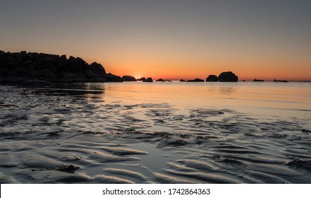 Southern coast of Finnish Gulf. Sand dunes with wave pattern. Baltic Sea water reflecting orange morning sky. Smooth transparent water, dark rocks. Blue hour turning to golden period. Estonia, Baltic
