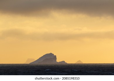 Southern Ocean, Near South Georgia. An Orange Sunset Gives An Eerie Feel To The Icebergs Just Offshore.