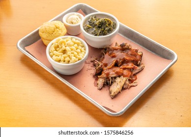 Southern Pulled Pork Platter With Bbq Sauce, And Traditional Barbecue Sides Of Corn Bread, Macaroni And Cheese, And Collard Greens.