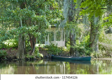 A Southern Scene With Gazebo, Pond, Canoe, And Cypress Trees.