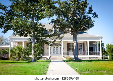 Southern Style Cottage With A Large Front Porch And Trees Along The Walkway To The Front Door.