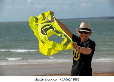 Southsea, Hampshire, England, UK. June 2020.  Woman Wearing Social Distancing T Shirt And Keep Your Distance Hi Vis Vest On A Windy Day On The Beach At Southsea