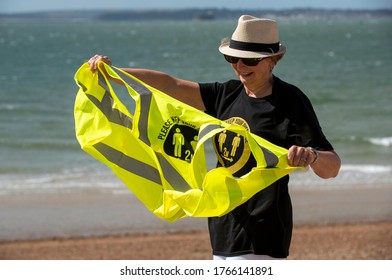 Southsea, Hampshire, England, UK. June 2020.  Woman Wearing Social Distancing T Shirt And Keep Your Distance Hi Vis Vest On A Windy Day On The Beach At Southsea