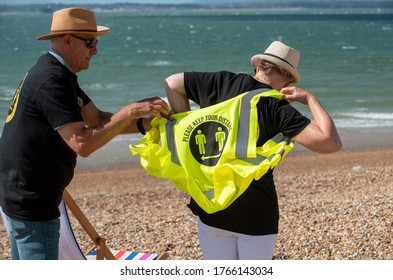 Southsea, Hampshire, England, UK. June 2020.  Woman Wearing Social Distancing T Shirt And Keep Your Distance Hi Vis Vest On A Windy Day On The Beach At Southsea