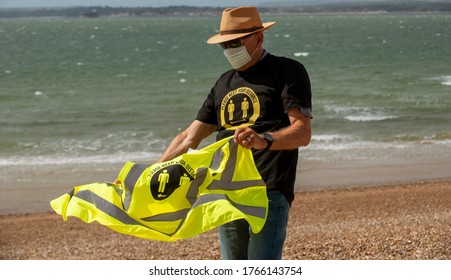 Southsea, Hampshire, England, UK. June 2020.  Man Wearing A Mask And Social Distancing T Shirt And Keep Your Distance Hi Vis Vest On A Windy Day On The Beach At Southsea