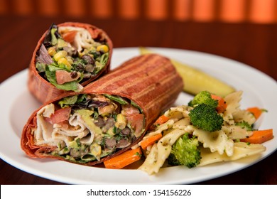 Southwest Chicken Wrap Sliced In Half On A White Paper Plate With A Side Of Pasta Salad.