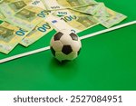 A souvenir soccer ball against a background of hundred-euro banknotes on a green background, sports betting, football match bets, sports betting, bookmaker bets, яяbetting odds.