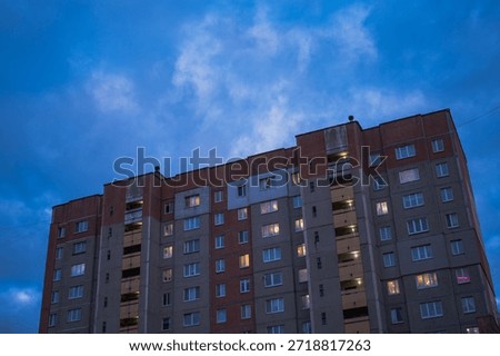 Soviet era panel apartment block in Minsk shows stairwell towers and uniform windows at twilight, some lit against the evening sky, viewed low and slightly tilted.