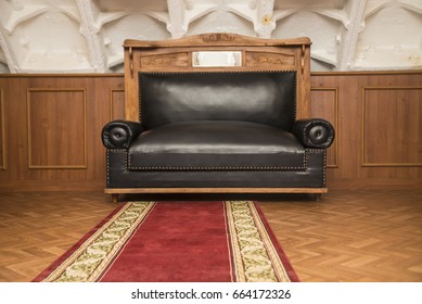 Soviet Union Retro Brown Leather Couch With Red Carpet On Wooden Floor. Interior Background Of 30th, 40th Empire Styled. Ussr Interior Background. No People. 