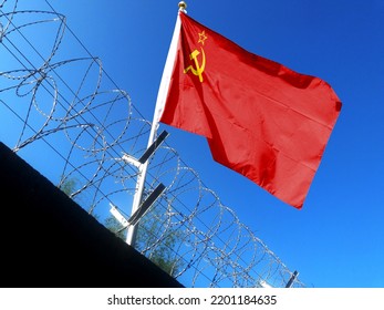 The Soviet-Russian flag hangs in the cloudy sky outside the prison's barbed wire. waving in the sky