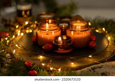 Soy candles burn in glass jars. Comfort at home. Candle in a brown jar. Scent and light. Scented handmade candle. Aroma therapy. Christmas tree and winter mood. Cozy decor. Festive garland decoration - Powered by Shutterstock