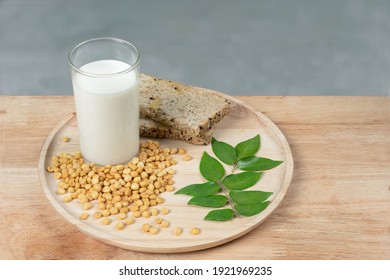 Soy milk in a glass, green leaf, soybeans in a bowl on a napkin against the background of a light wooden board

