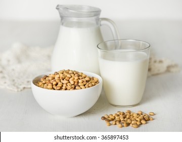 Soy milk in a glass and jar, soybeans on a white table