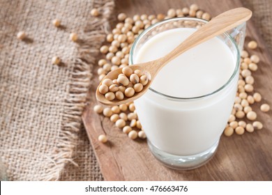 Soy milk on wooden background and sack texture with spoon full of soybeans or soya beans placed on top of a glass, selective focus
