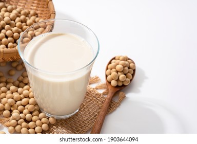 Soy milk and soybeans in a glass and a wooden spoon on a white background with copy space