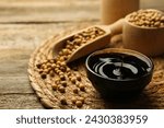 Soy sauce in bowl and beans on wooden table, closeup. Space for text