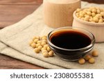 Soy sauce in bowl and soybeans on wooden table, closeup