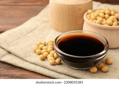 Soy sauce in bowl and soybeans on wooden table, closeup