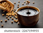 soy sauce drop falling from flying soybeans in wooden bowl and created splash on black stone background. Traditional asian condiment. Natural product concept