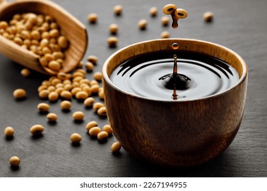 soy sauce drop falling from flying soybeans in wooden bowl and created splash on black stone background. Traditional asian condiment. Natural product concept - Shutterstock ID 2267194955