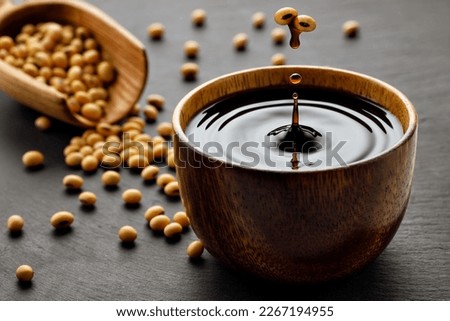 soy sauce drop falling from flying soybeans in wooden bowl and created splash on black stone background. Traditional asian condiment. Natural product concept Stock foto © 