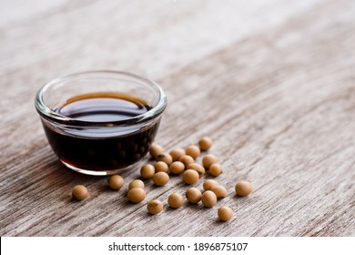 Soy sauce in glass bowl with soybeans isolated on wooden table background. 