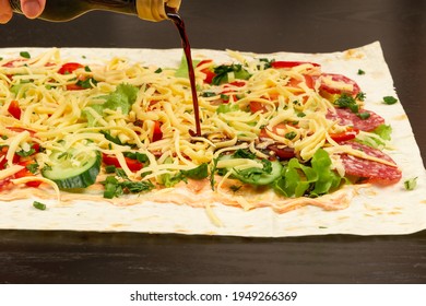 Soy Sauce Is Poured From The Bottle On The Unwrapped Shawarma With Fresh Herbs, Cheese And Vegetables On The Background Of A Black Wooden Table