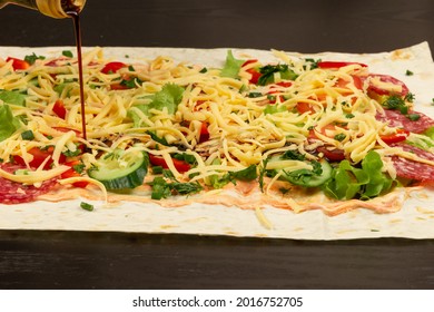 Soy Sauce Is Poured From The Bottle On The Unwrapped Shawarma With Fresh Herbs, Cheese And Vegetables On The Background Of A Black Wooden Table