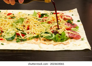 Soy Sauce Is Poured From The Bottle On The Unwrapped Shawarma With Fresh Herbs, Cheese And Vegetables On The Background Of A Black Wooden Table