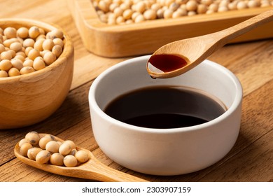 Soy sauce in wooden spoon and soy bean on wooden table