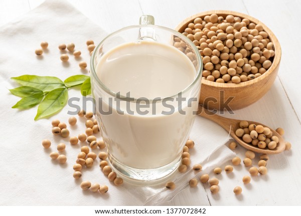 Soy or soya milk in a glass with soybeans in\
wooden bowl background
