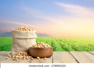 Soybeans in wooden bowl and cotton bag on wooden table with blur green soybean field and morning light background.