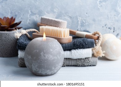 Komposition mit Badebomben, Körperbürsten und Handtüchern. Aromatherapie-Arrangement, Zen-Stillleben auf hellgrauem Hintergrund mit heller Kerze