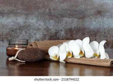 Spa composition with candles, towel, orchid and pumice stone against a brown background.