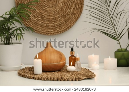 Spa composition. Essential oil diffuser, cosmetic products, burning candles and plants on table