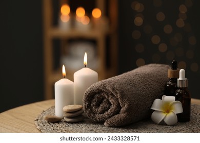 Spa composition. Rolled towel, cosmetic products, stones, burning candles and plumeria flower on table indoors, closeup. Space for text - Powered by Shutterstock