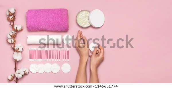 Spa concept. Cotton pads for removal makeup with\
woman hands, cotton branch, cotton pads, ear sticks, pink towel.\
Cotton Cosmetic Makeup Removers Tampons. Flat lay background Top\
view copy space