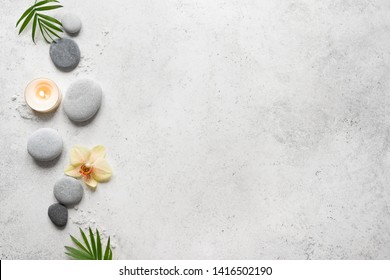 Spa concept on white stone background, palm leaves, flower, candle and zen like grey stones, top view, copy space.