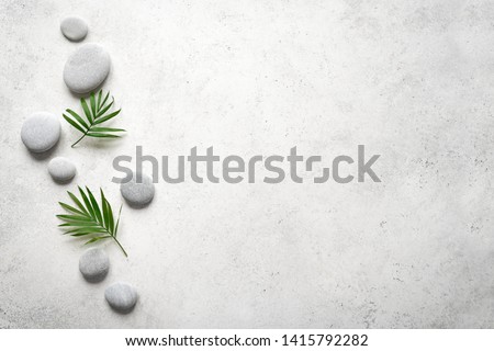 Spa concept on white stone background, palm leaves and zen like grey stones, top view, copy space. 
