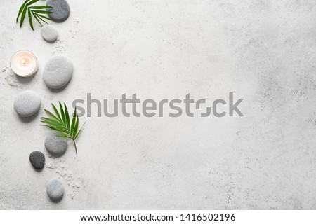 Spa concept on white stone background, palm leaves, candle and zen like grey stones, top view, copy space.