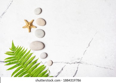 Spa Concept. Top View Of Grey Sea Stones, Starfish And Green Fern On White Marble Background With Copy Space