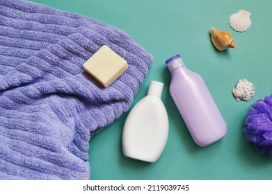 Spa cosmetics, natural bath products view from above flat lay photography. Purple soft towel, white shampoo bottle, shower gel, soap bar on a green background