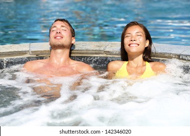 Spa couple relaxing enjoying jacuzzi hot tub bubble bath outdoors on romantic summer vacation travel holidays or honeymoon. Young interracial couple in love, Asian woman, Caucasian man.