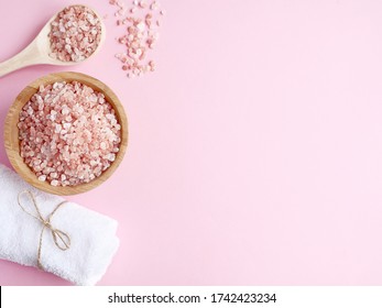 Spa flatlay composition. Sea salt in wooden jar and scattered from spoon, bath towel on pink background. Copyspace, top view. Home care concept, relax and rest, bath procedure