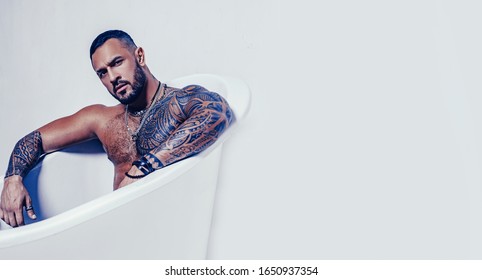 spa and hygiene. time to relax in bathroom. confidence charisma. brutal sportsman. steroids. muscular man with athletic body. sexy abs of tattoo man in bath tub. stay clean and fresh. copy space.