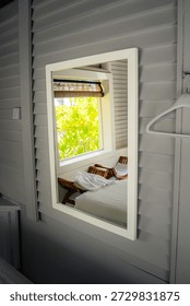 A spa cabana’s interior is reflected in a wall mirror, creating a tranquil sanctuary. Crisp linens and tropical foliage hint at a luxury wellness retreat—a minimalist space for relaxation.