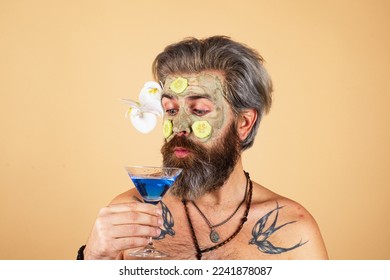 Spa man with clay mask and cucumber slices on face drink cocktail. Spa, dermatology, wellness and facial treatment concept. Man having cosmetic moisturizing mask, isolated studio background. - Powered by Shutterstock