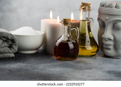 Spa massage relax composition setting. Natural essence oils, sea salt, towel, candles, Buddha head statue on gray background. - Powered by Shutterstock