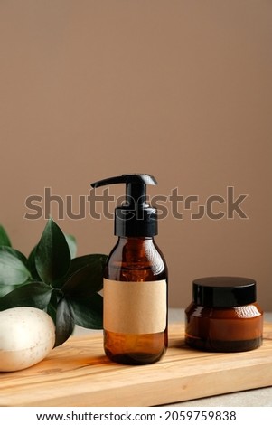 SPA natural organic cosmetics for personal hygiene. Amber glass pump cosmetic bottle, jar of moisturizer cream, homemade soap and green leaf on wooden board in bathroom.